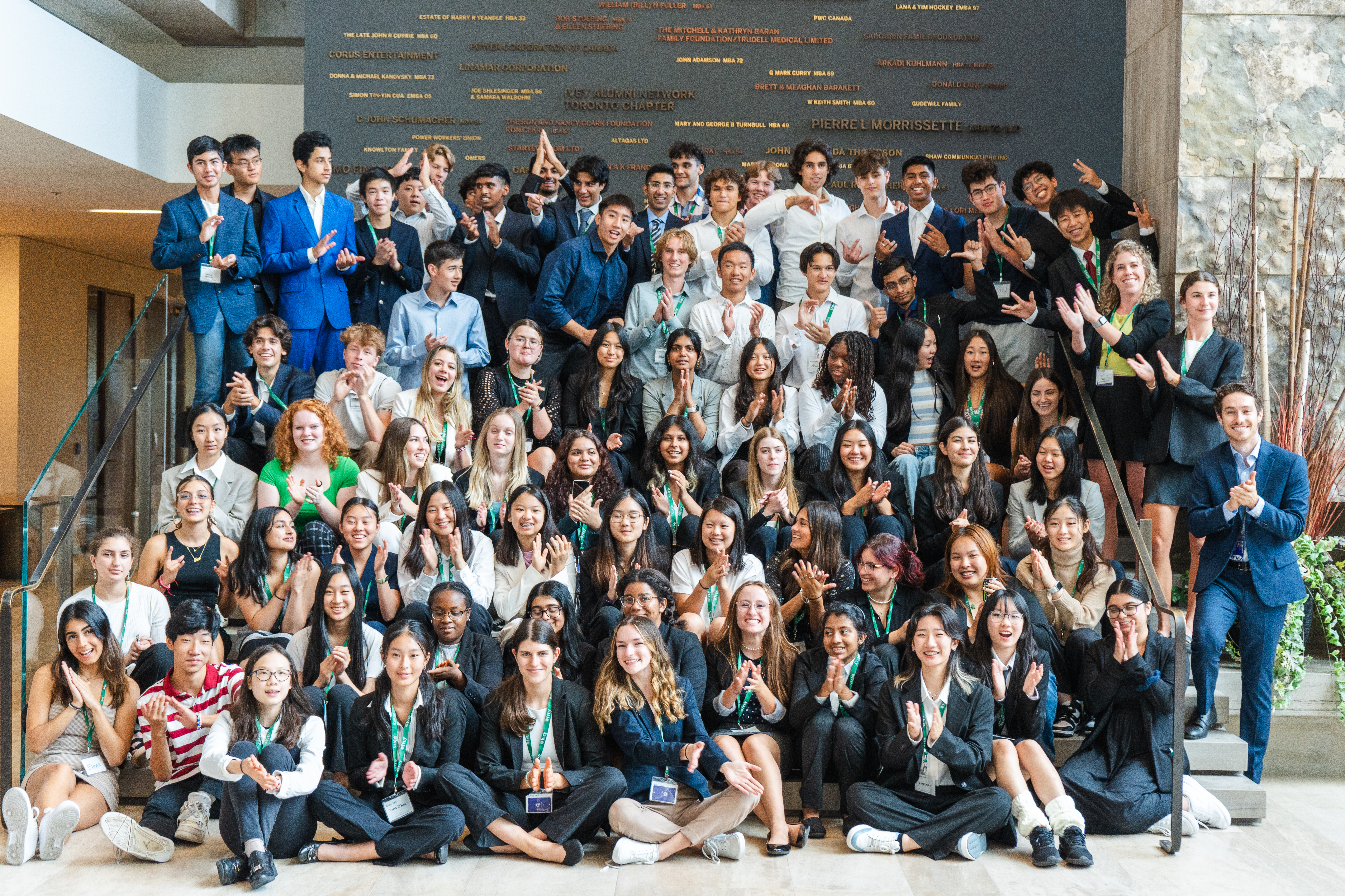 A group of 76 high school students, all wearing business attire, on the main steps in the Ivey Building in front of the Ivey Donor Wall.