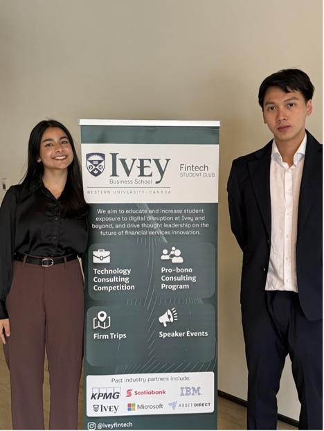 Two students standing and smiling in front of the Ivey FinTech Club banner