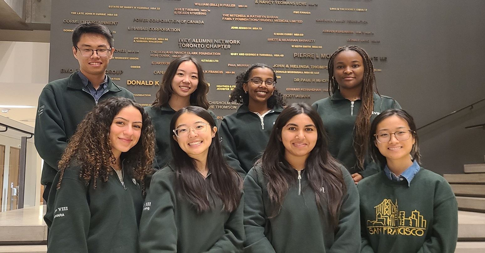 The eight members of the ICEC executive team stood in two rooms in front of the Ivey Donor wall in the main hall.  Each student wears an Ivey green sweater.