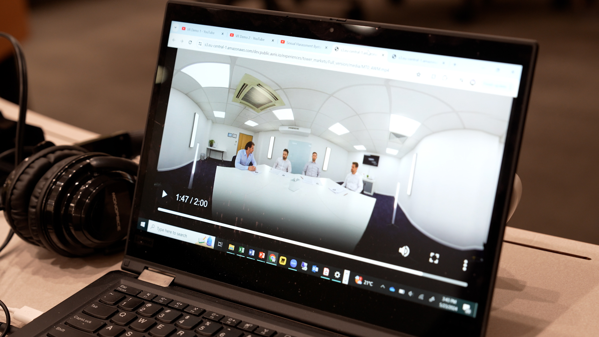 An open laptop showing the optimized view of  a VR simulation featuring a team meeting.  There are a set of headphones to the left of the laptop.