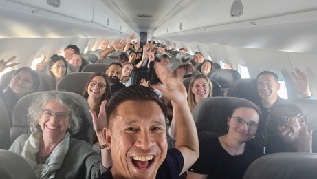 Members of Ivey's executive MBA class smiling and waving at the camera from inside of their airplane on the way to Brazil