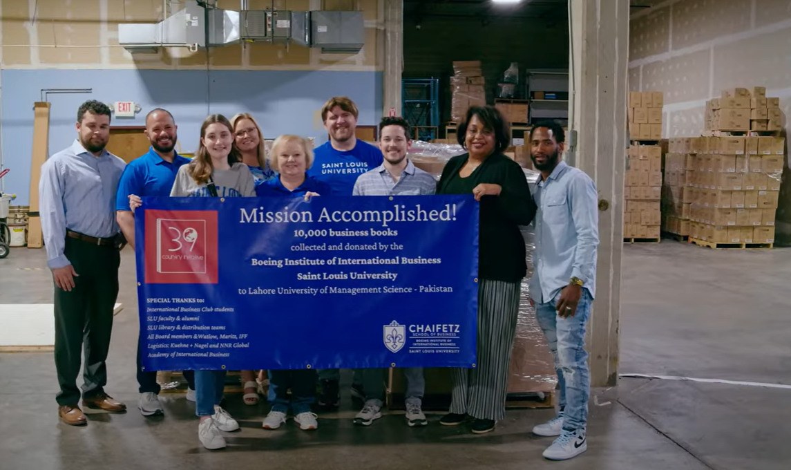 The team of 9 faculty and students holds up a banner that reads Mission Accomplished