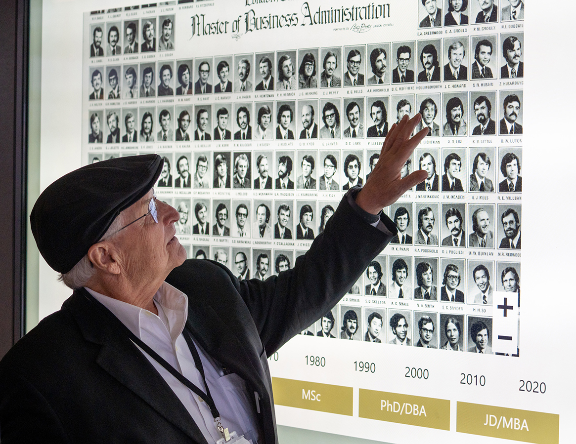 An alumnus at Homecoming 2024 scrolls through class composite photos on a large screen.