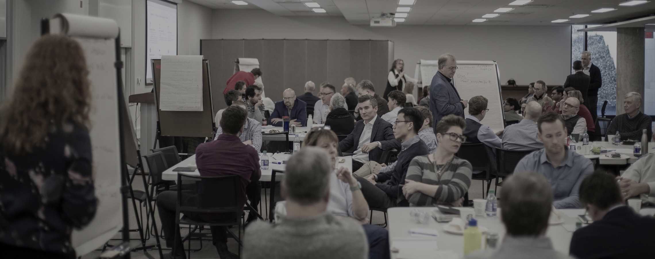 A meeting room full of Ivey Professors in small groups, working with flip charts and post-it notes